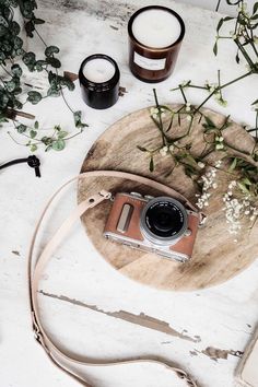 a camera sitting on top of a wooden table next to some candles and greenery