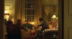 a group of people sitting around a table in a living room next to a window