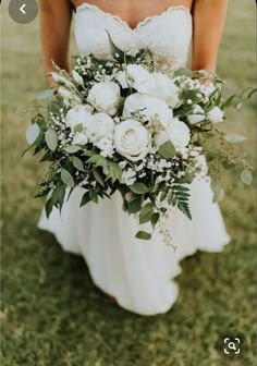 a bride holding a bouquet of white flowers and greenery in her hands on the grass