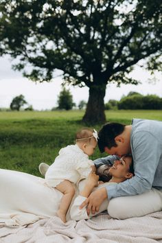 a man and woman laying on top of a blanket holding a baby