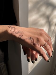 a woman's hand with a tattoo on her left arm and fingers, in front of a window