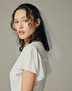 a woman wearing a white wedding dress and veil posing for a photo in front of a gray background