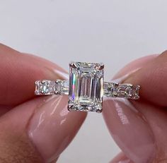 a woman's hand holding an emerald and baguette diamond ring with three side stones