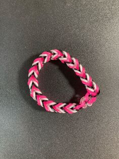 a pink and white braided bracelet sitting on top of a gray table next to a cell phone