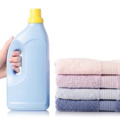 a hand holding a bottle of detergent next to towels