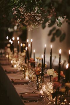 a long table is set with candles and flowers in vases on the tables, along with other place settings