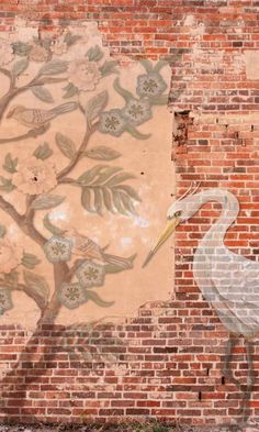 a white bird standing in front of a brick wall with flowers painted on it's side