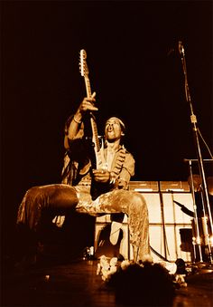 a man sitting on top of a stage with a guitar in his hand and another person standing next to him
