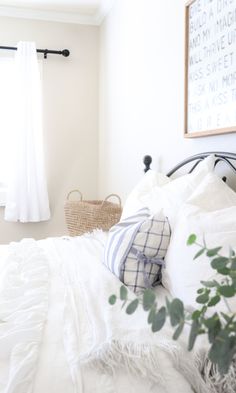 a bed with white sheets and pillows next to a plant in a basket on top of it