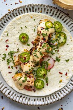 a tortilla topped with chicken, jalapenos and sauce on a plate