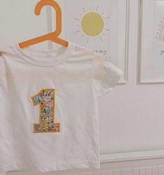 Liberty London Birthday Number T-shirt |  Gift Idea | Liberty of London Fabric | Party Outfit | Girls & Boys Party |Custom Made Birthday T-shirt  A beautiful Liberty London with an embroidered  Number for birthday with outline contrasting Thread. (or you can choose your own just ask, you can message me when you order and I will do my best to match it :) 1.Choose the Colour T-Shirt  2. Choose the Liberty Fabric 3.Choose Size of T-Shirt 4.Choose Number 5. Choose the Thread or I can choose a contra Summer Graphic Tee With Number Print, Summer Crew Neck Top With Number Print, Cute Number Print Tops For Birthday, Summer Birthday Top With Cartoon Print, Cute Tops With Number Print For Birthday, Summer Cartoon Print Tops For Birthday, Crew Neck Top With Cartoon Print For First Birthday, Cotton Graphic Print T-shirt For Birthday, Summer Cotton Tops With Number Print