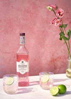 a bottle of bloom gin next to two glasses with limes and flowers in the background