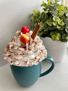 a cup filled with whipped cream and topped with an apple on top, next to a potted plant