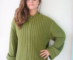 a woman in a green sweater poses for the camera with her hands on her hips