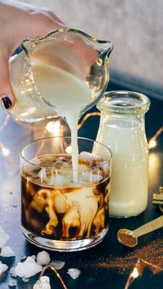 a person pouring liquid into a glass filled with ice and marshmallows on a table