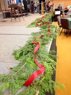 a long line of christmas greenery with red ribbon on the side and people sitting at tables in the background