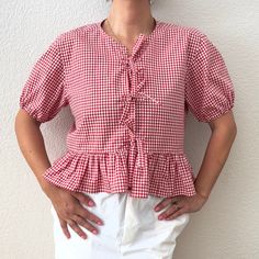 a woman standing in front of a white wall wearing a red and white checkered top