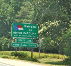 a welcome sign to north carolina and state line on the side of a road with trees in the background