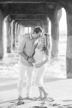 a pregnant couple kissing under an old pier