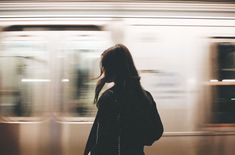 a woman standing in front of a train at a subway station with motion blurry behind her