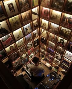 a man sitting at a desk in front of a wall full of records