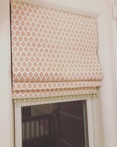 an open window with a pink and white roman blind