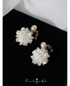 two white flowers and pearls are on a black surface with gold ear wires in the middle