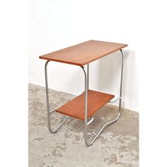 a small wooden table sitting on top of a cement floor next to a white wall