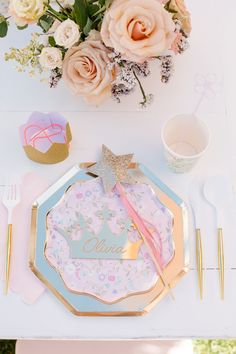 a table set up with pink and blue plates, napkins, silverware and flowers