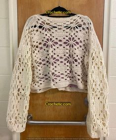 a white crocheted sweater hanging on a wooden door with the words crocheting com written below it