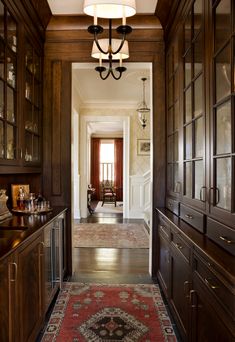 a hallway with wood paneling and glass doors leading to a dining room area that has a red rug on the floor