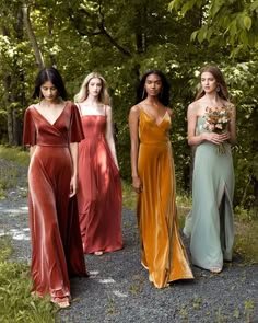 four women in long dresses standing on gravel path with trees in the backgroud