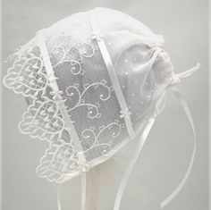 "This pretty bonnet is perfect for all of baby's formal events.  It is made with two layers of sheer fabric, edged with a heart motif lace.  There is a ribbon adjustable back closure and satin ribbon ties.   3-6m      16-18\" 9-12m    18-20\" Hand wash, line dry, cool iron (use a press cloth) All components are CPSIA compliant. All items are made in a smoke and pet free environment." Fitted White Bonnet With Lace Trim, Adjustable Lace Wedding Bonnet, Elegant Lace Bonnet With Lace Trim, Fitted White Bonnet For Baptism, White Fitted Bonnet For Baptism, White Adjustable Lace Bonnet, White Lace Adjustable Bonnet, White Fitted Hat With Lace Trim, Fitted Cream Bonnet With Lace Trim