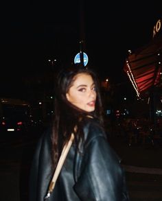 a woman walking down the street at night wearing a leather jacket and carrying a purse