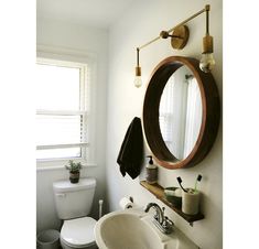 a white toilet sitting next to a bathroom sink under a round mirror on a wall