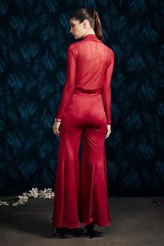 a woman in a red jumpsuit standing against a blue wall with leaves on it