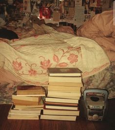 a pile of books sitting on top of a wooden floor next to a bed covered in sheets