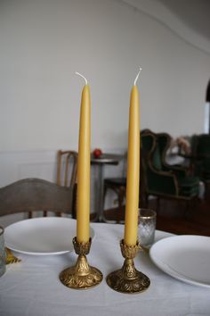 two yellow candles sitting on top of a white tablecloth covered table with plates and silverware