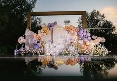 balloons and flowers decorate the backdrop for an outdoor birthday party at dusk or dawn in front of a large mirror