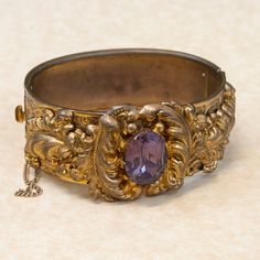 This antique Victorian etched gold plate bangle bracelet is heavy with details and a beautiful purple glass stone.  This is quite a statement piece from an amazing period of time long ago. This bangle really depicts the style and appreciation of craftsmanship of the time period it was made in. What an unusual and wonderful piece to own and enjoy!Antique BraceletVictorianGlassGold PlatedBangle BraceletDimensions: Will fit a 7" inch wrist and is 1" inch widePlease read our shop policies prior to p Luxury Victorian Etched Bangle, Antique Gold Engraved Bracelet, Antique Gold Bracelet In Antique Style, Antique Gold Bracelet With Intricate Design, Antique Gold Antique Bracelet, Antique Bronze Bracelets For Formal Occasions, Antique Bronze Bracelet For Wedding, Victorian Antique Gold Bracelet, Antique Gold Bangle Bracelet