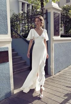 a woman in a white dress is walking down the street with her hand on her hip