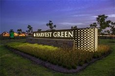 the sign for harvest green is lit up at night in front of some grass and trees