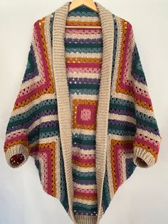 a multicolored knitted cardigan sweater hanging on a wooden hanger with a white background