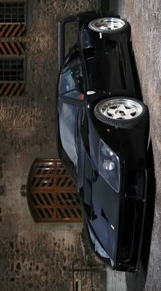 a black sports car parked on the side of a road next to a tree trunk