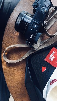 a camera sitting on top of a wooden table next to a bag and coffee cup