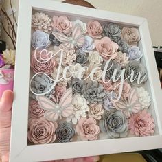 a person holding up a shadow box with paper flowers in it and the word love spelled out