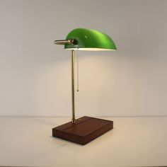 a green table lamp sitting on top of a wooden stand next to a white wall