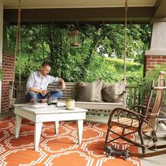 a man sitting on a porch swing with his coffee table and books in front of him