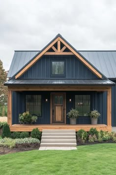 a blue house with a metal roof and two plants on the front porch, along with steps leading up to the front door