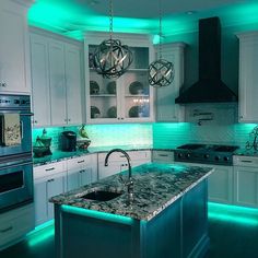 a kitchen with white cabinets and green lights on the counter tops, along with an island in the middle